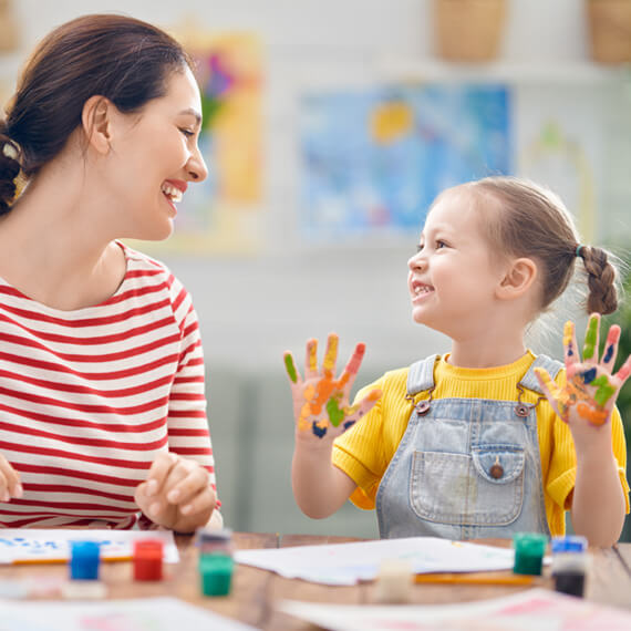 Mother and daughter smiling with painted hands, a family-centered early intervention activity