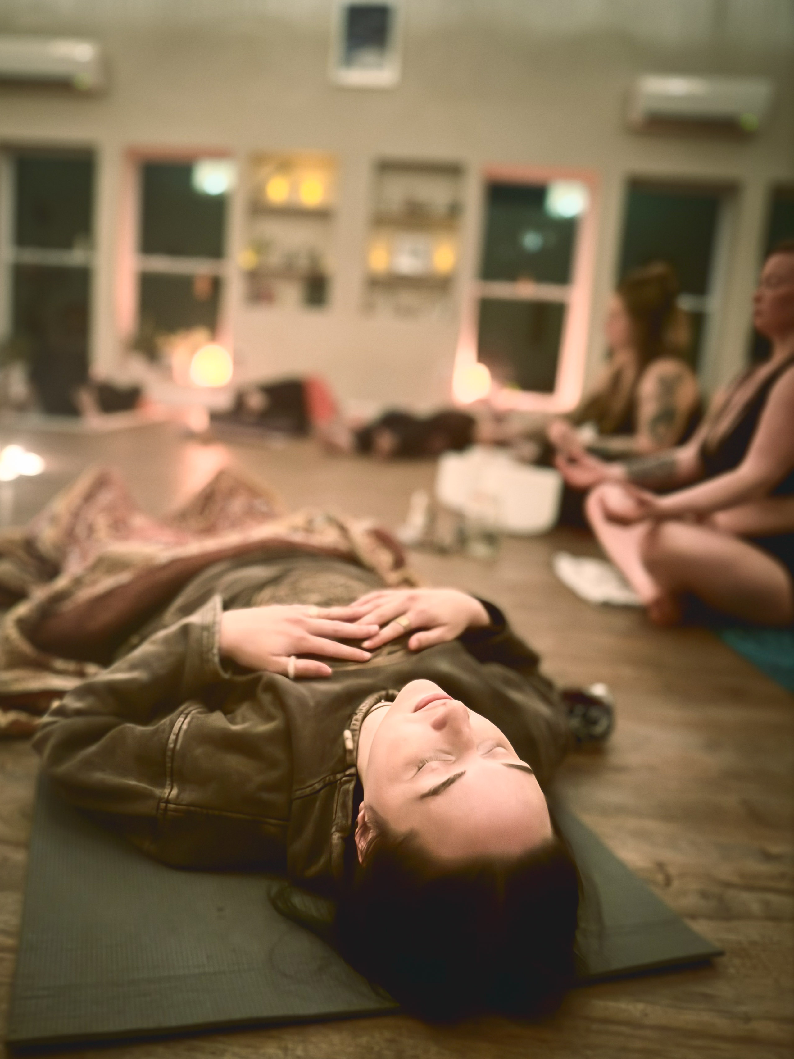Group guided breathwork session, participants resting on mats in a candlelit room