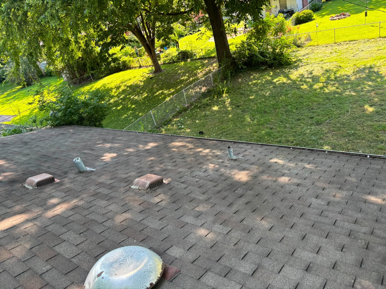 Close-up view of a dark shingled roof next to a gutter with mesh, white siding, and red brick wall.