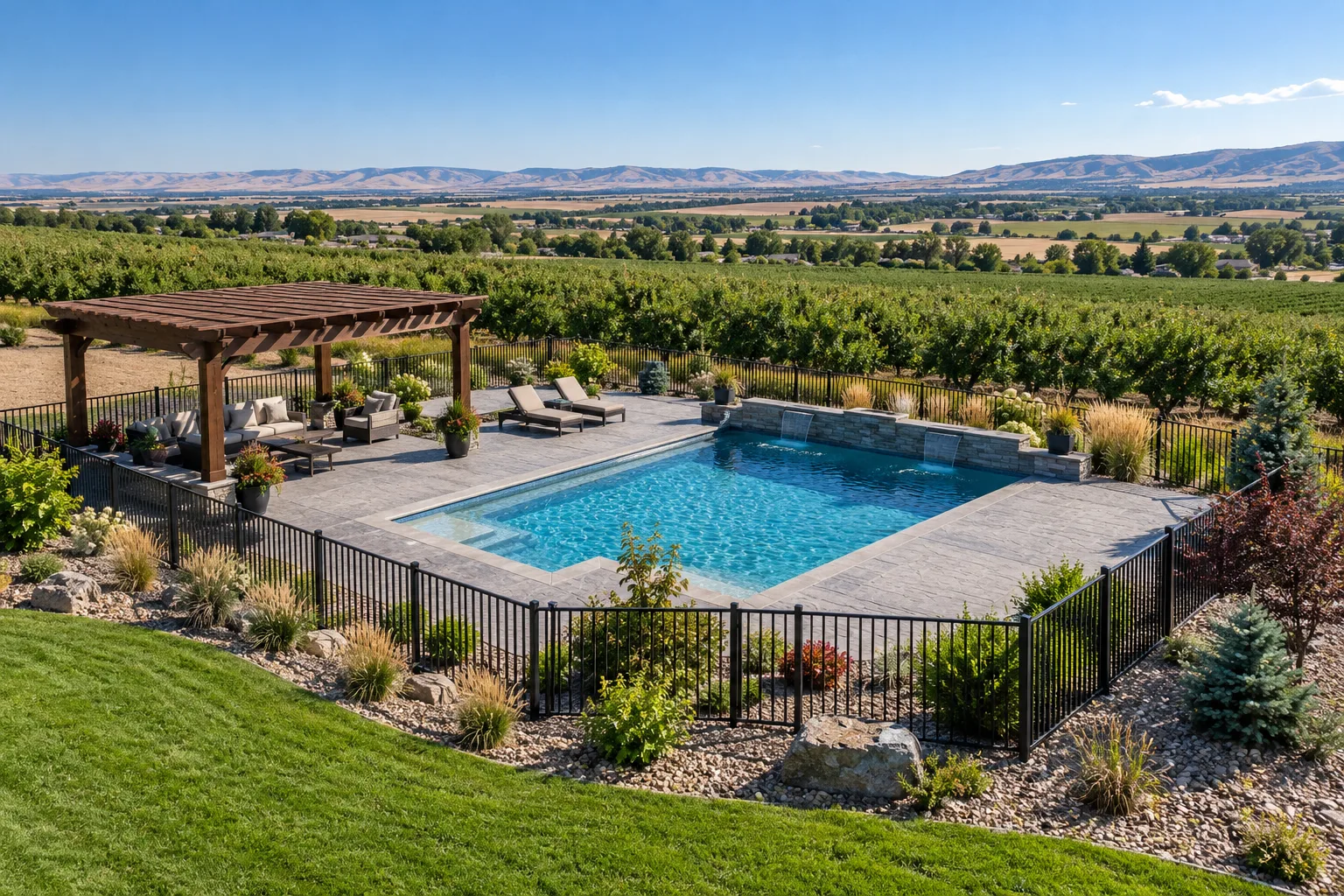 Wide view of acreage backyard pool area with concrete deck, fencing, lawn, and orchard rows near Caldwell, Idaho