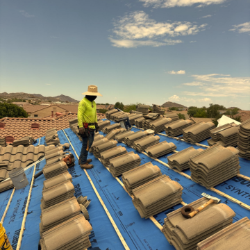 Professional roofer installing new concrete roof tiles over blue synthetic underlayment on a residential home in Chandler, AZ.