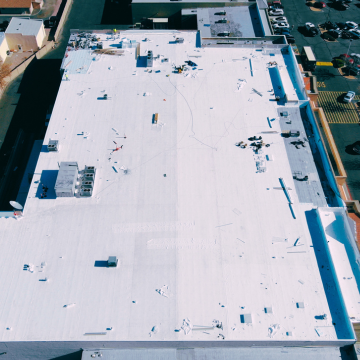 Aerial drone view of a large white commercial flat roof installation in Mesa, AZ, showing HVAC units and professional roofing equipment.