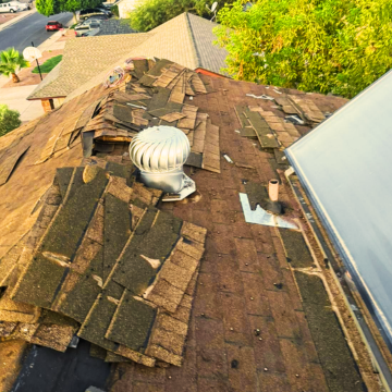Damaged asphalt shingles and a wind turbine vent on a residential roof in Queen Creek, AZ, showing severe sun and wind wear.