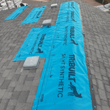 High-quality blue synthetic underlayment secured tightly over a shingle roof to provide temporary weatherproofing, showcasing a quick-response emergency roof repair contractor queen creek az tarping service.