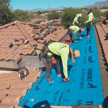 Professional roofers in queen creek installing protective synthetic underlayment on a residential clay tile roof under the Arizona sun.