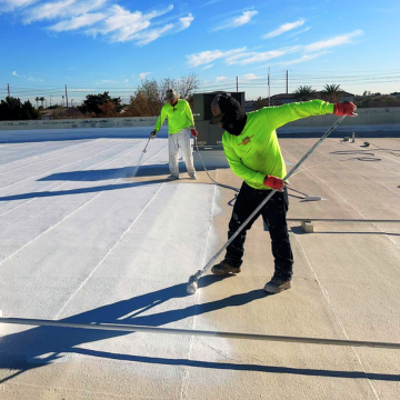 Contractors applying protective white foam roofing coating on a commercial building managed by a roofing company Scottsdale AZ.