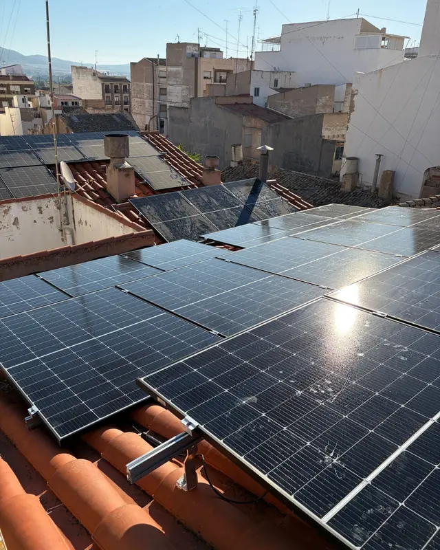 Placas solares sobre tejados de teja del casco urbano, con la sierra al fondo