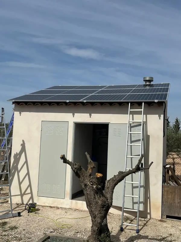 Placas solares sobre el tejado de una caseta, con la escalera de la obra apoyada