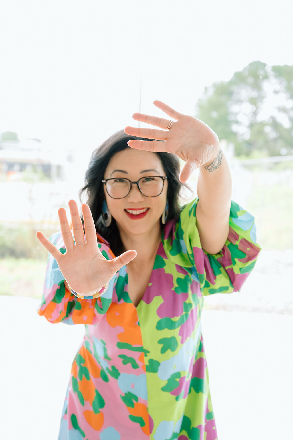 Sora Schilling in a bright patterned dress, framing the camera with her hands and laughing