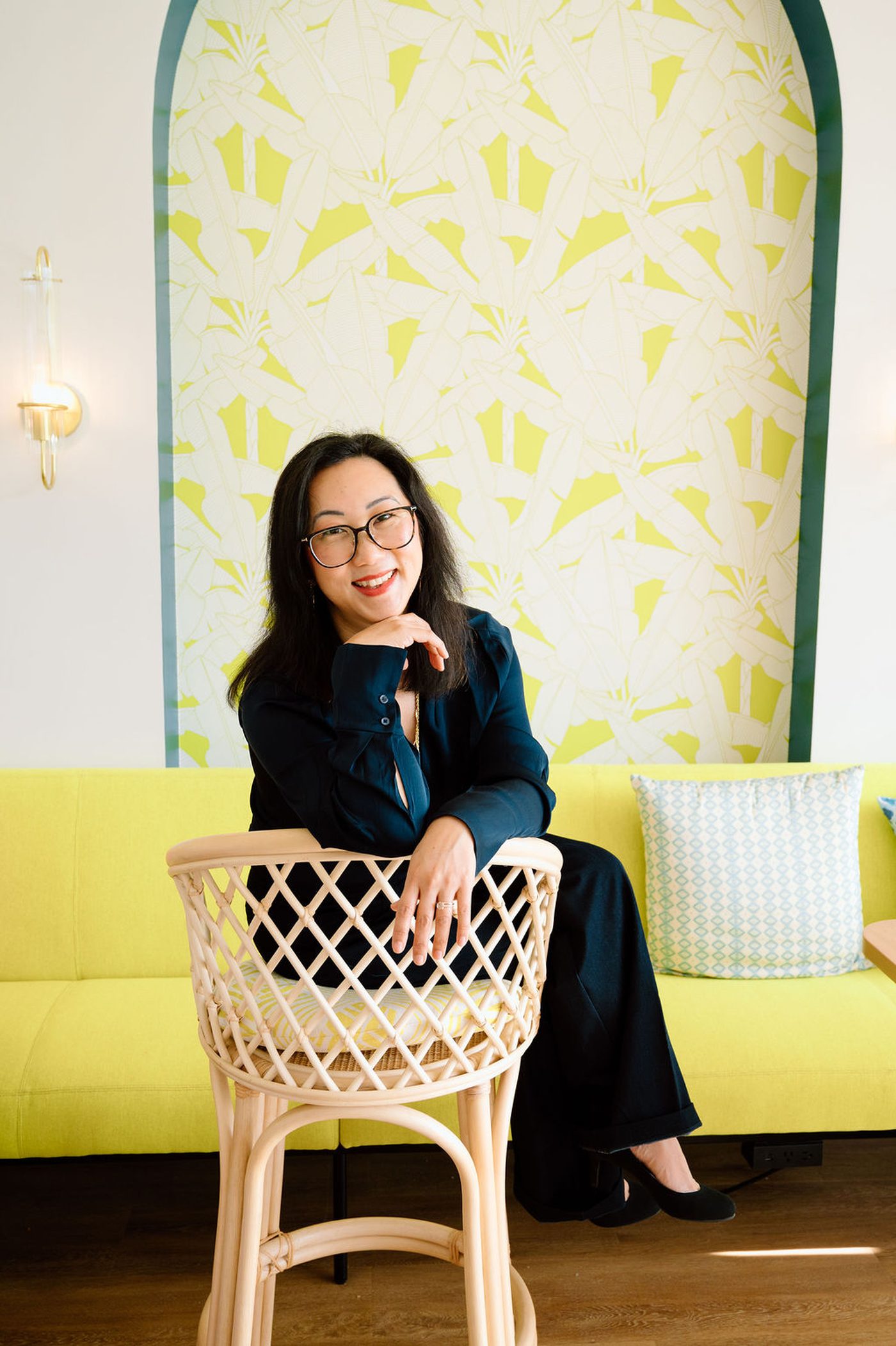 Sora Schilling seated in a navy suit against a yellow and ivory setting