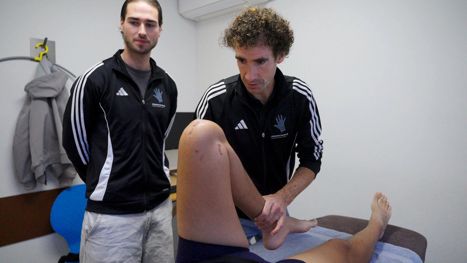 Martijn van de Rijt behandelt de knie van een patiënt terwijl een collega meekijkt