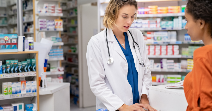 Un farmacéutico conversando con un cliente mientras revisa la lista de medicamentos prescritos y los gastos de copago. Un farmacéutico conversando con un cliente mientras revisa la lista de medicamentos prescritos y los gastos de copago.