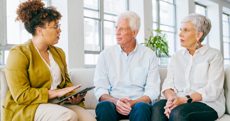 A Medicare insurance advisor explaining the different parts of Medicare to a retired couple in an office. A Medicare insurance advisor explaining the different parts of Medicare to a retired couple in an office.