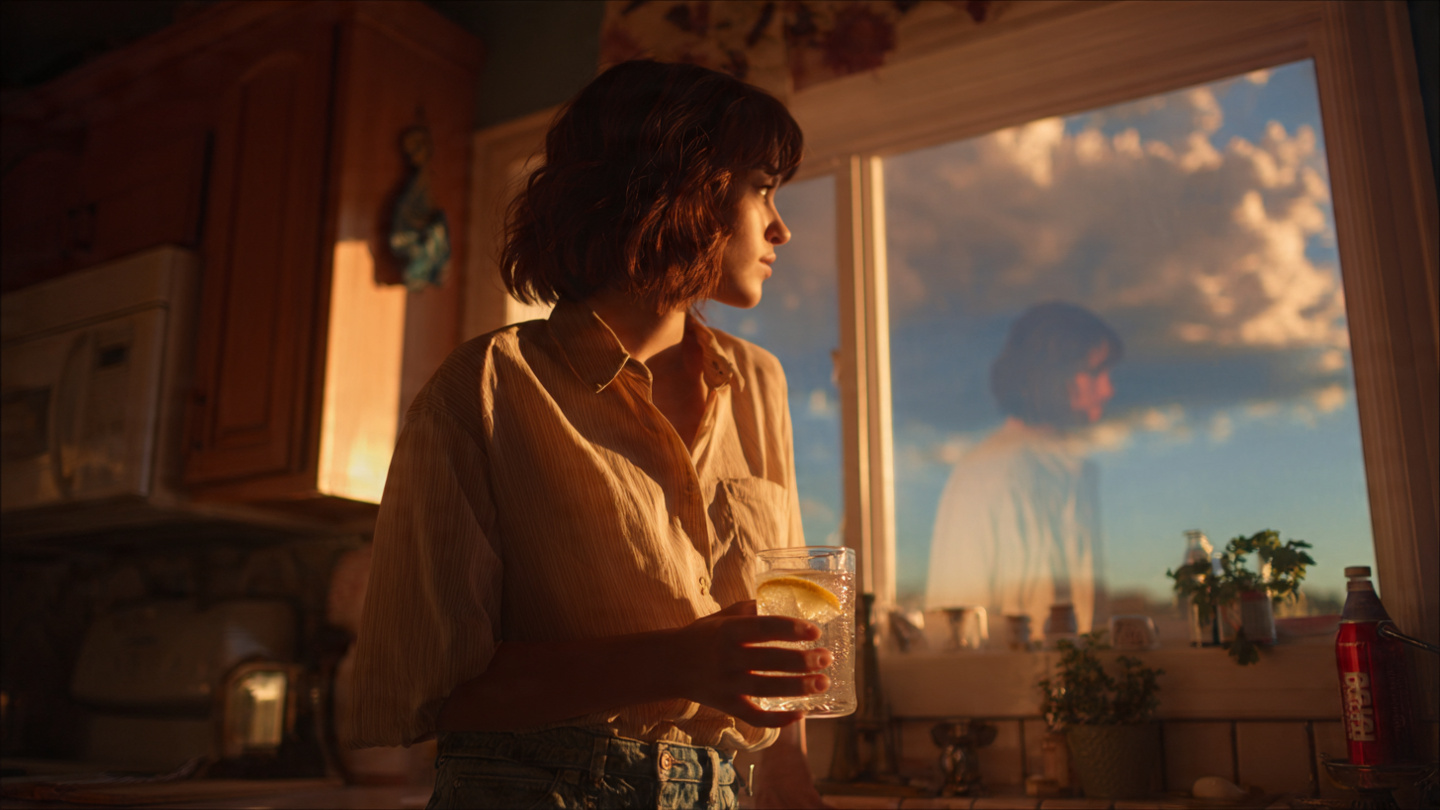 A person standing in a kitchen at sunrise, holding a glass of clear water with lemon, looking out a window at a bright morning sky. Behind them, a faint ghost-like image of their former self reaching for a soda. Transition imagery—new identity forming. Warm, hopeful lighting. 