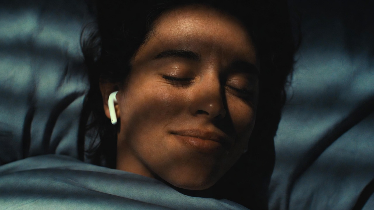 Dreamy, slightly surreal image of a person lying in bed at dawn, eyes closed, earbuds in, with faint glowing neural pathways or soft light visualized around their head, suggesting brainwave activity and reprogramming happening. The sun is just beginning to rise outside the window. The mood is mystical but grounded—science meets spirit. Theta waves gently visualized in soft gold and white light. Cinematic, aspirational, shot on medium format, warm tones, shallow depth of field, 8k resolution.