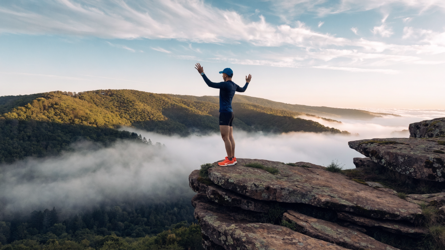 A man standing on a Cliff with his arms raised up overlooking Misty Valley and tree covered mountain tops A man standing on a Cliff with his arms raised up overlooking Misty Valley and tree covered mountain tops