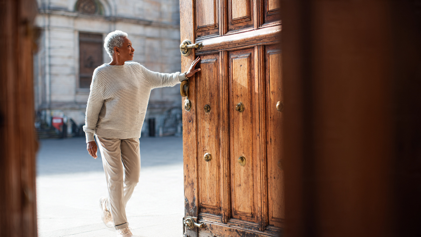 Senior woman pushing a very large wooden door looking surprised because it used to be heavy My kettlebell workouts must be paying off Senior woman pushing a very large wooden door looking surprised because it used to be heavy My kettlebell workouts must be paying off