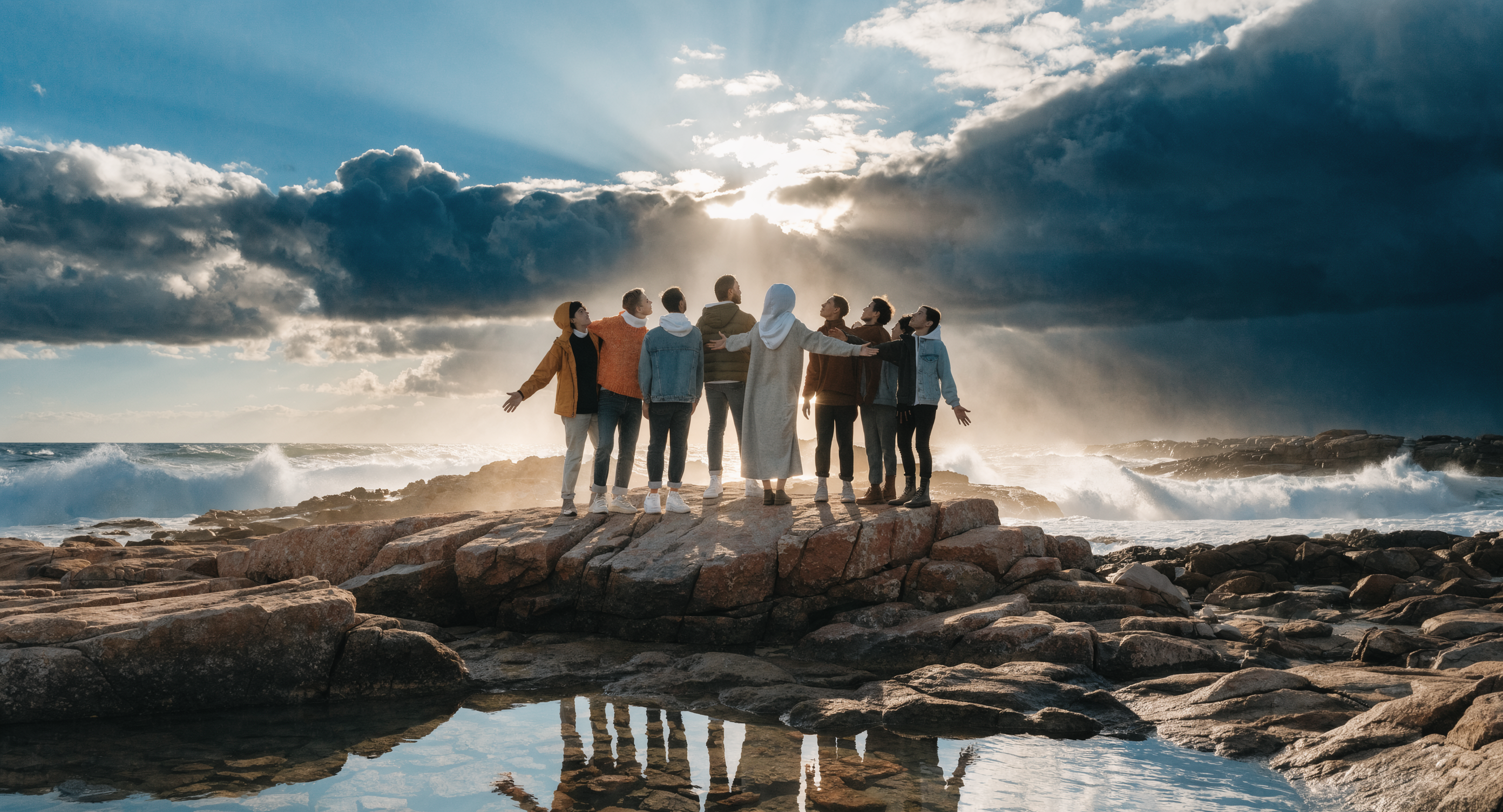 Photorealistic image of multiple diverse people standing together at sunrise, arms open or hands connected, golden light surrounding the group, representing consciousness community and collective intention, cinematic wide shot