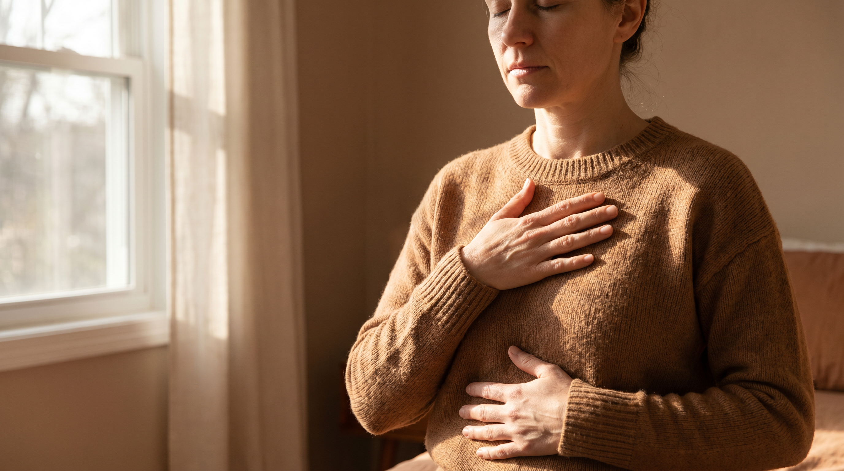 Photorealistic close-up of a person's hands gently placed on their own torso, one hand on the heart and one on the stomach, eyes closed in deep breathing, soft natural morning light streaming across their skin, conveying a sense of deep internal listening and embodiment.