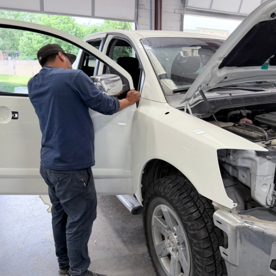 A collision repair tech adjusting the front passenger door on a fresh painted white truck