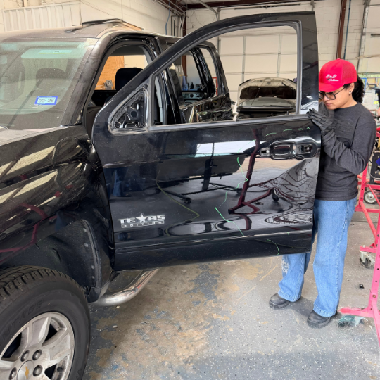 Professional female collision repair technician re-assembling the driver-side front door of a black Chevy truck