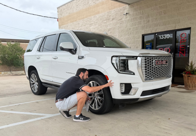 A B&D Collision professional in Mesquite inspecting the front bumper and wheel well of a white GMC SUV