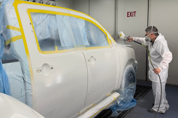 Professional auto body painter applying computerized color-matched white paint to a truck fender in a paint booth at B&D Collision in Mesquite, Texas.