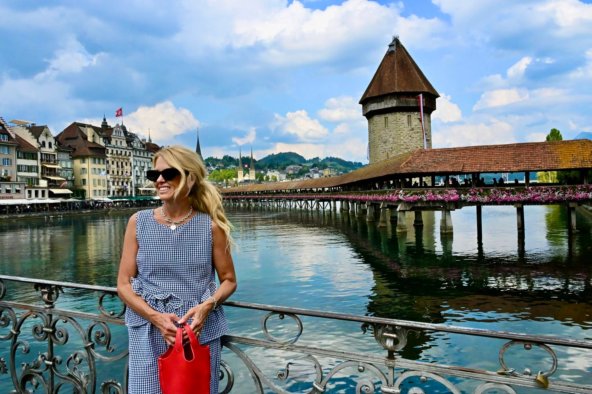 A woman smiling on a riverside bridge in Lucerne, Switzerland, with the historic Chapel Bridge and Water Tower and lakeside old town buildings in the background