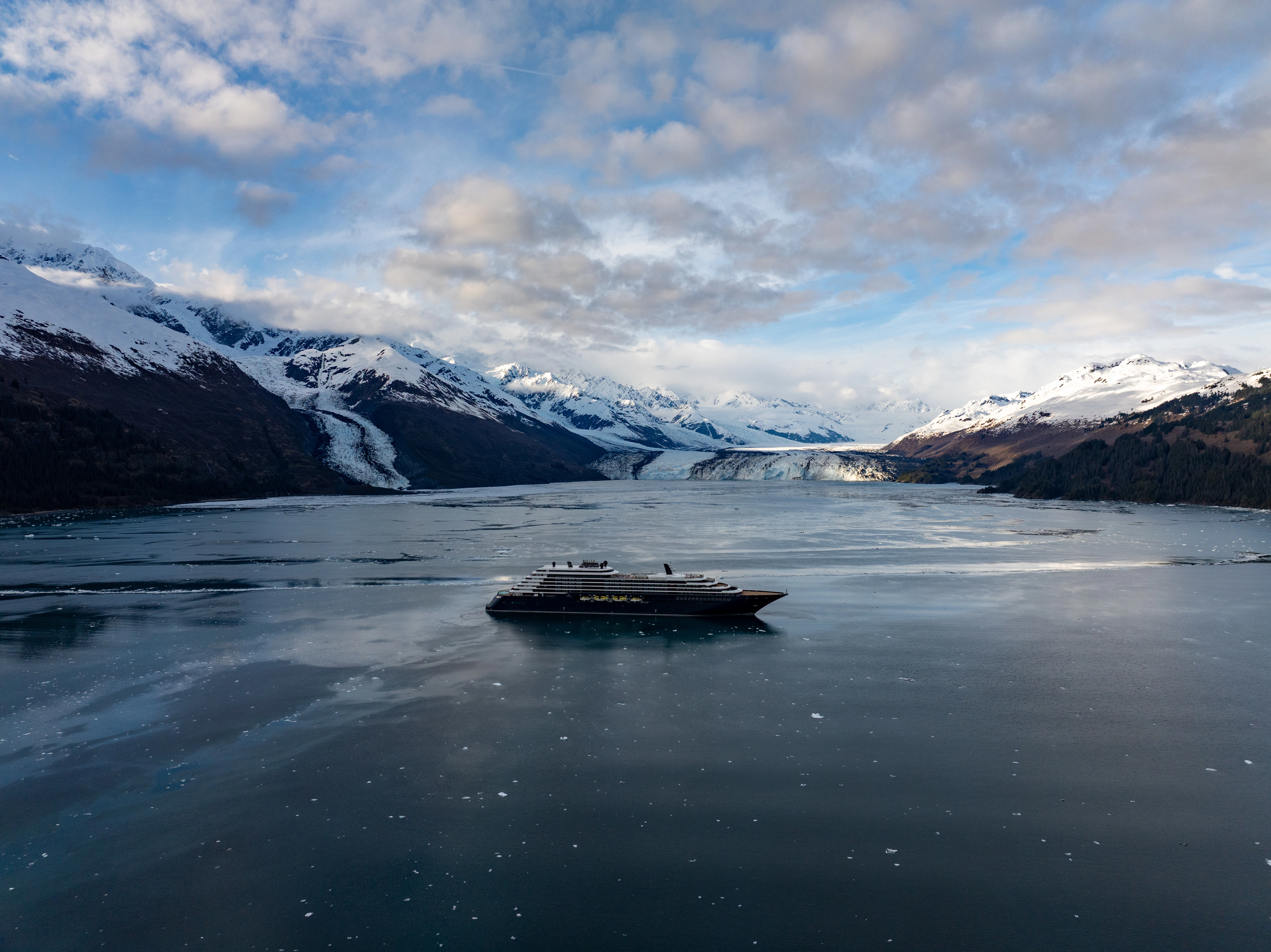 Luxury yacht cruising toward a glacier in Alaska surrounded by snow-capped mountains