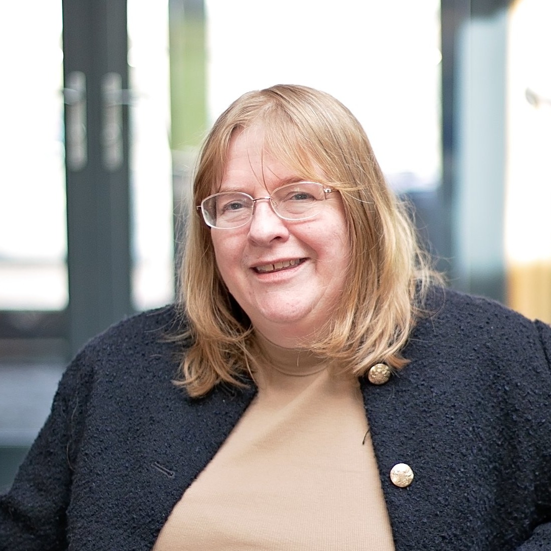 Kathryn Dunn, smiling at the camera, in a navy jacket in front of a window