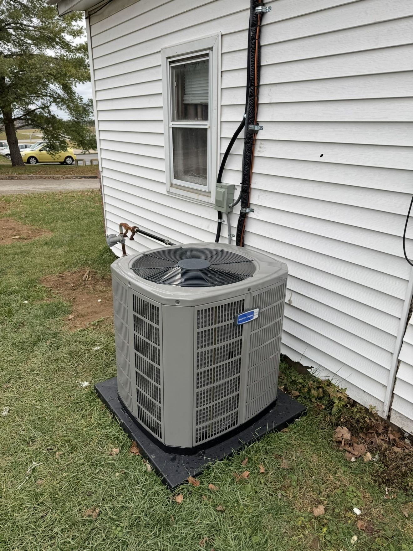 Newly installed American Standard outdoor AC condenser on a pad next to a white vinyl-sided house