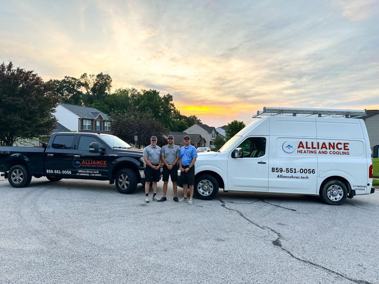 Three Alliance technicians standing between a company truck and van at sunset