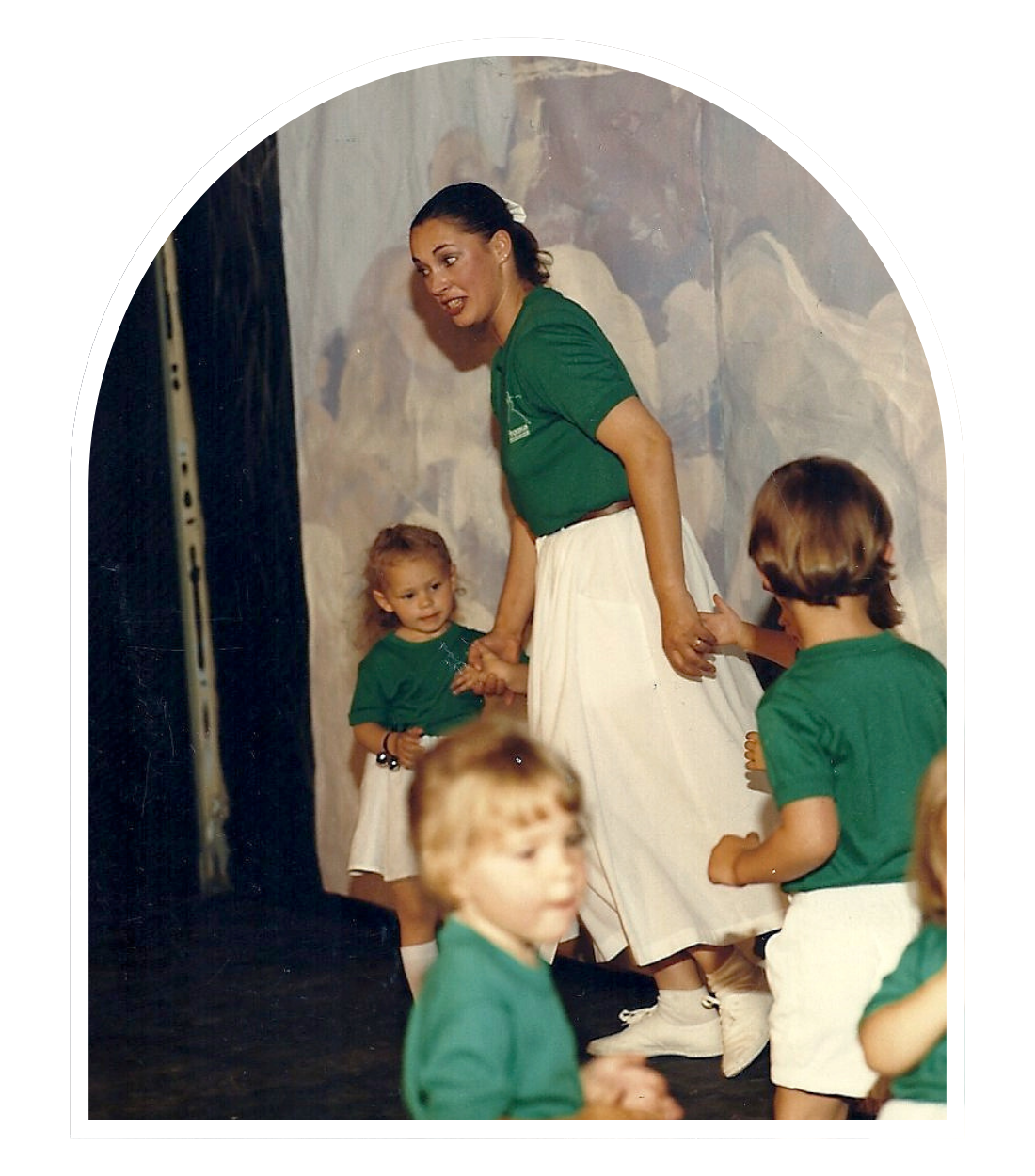 Vintage photo of Pegasus Dance recital - women in green shirt and white skirt leading young children in matching outfits in a dance show
