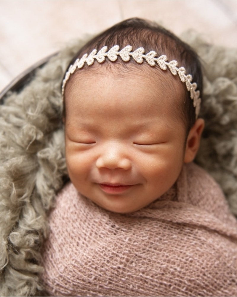 Smiling newborn in a pink wrap with a leaf headband