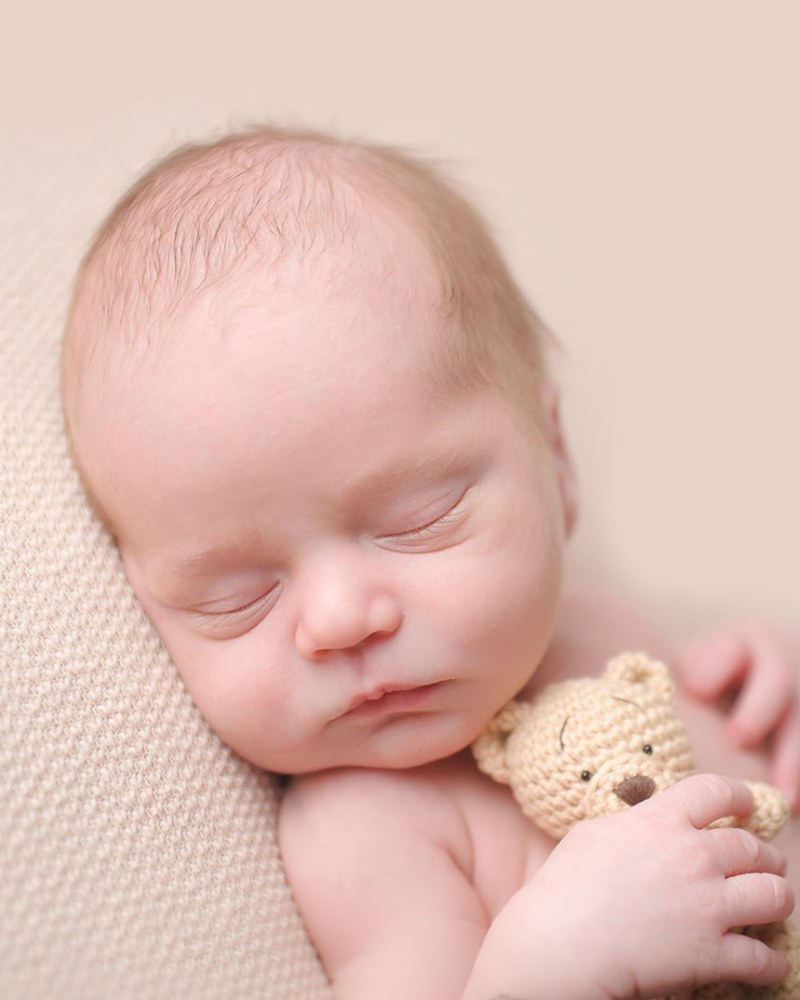 Sleeping newborn holding a knit teddy bear