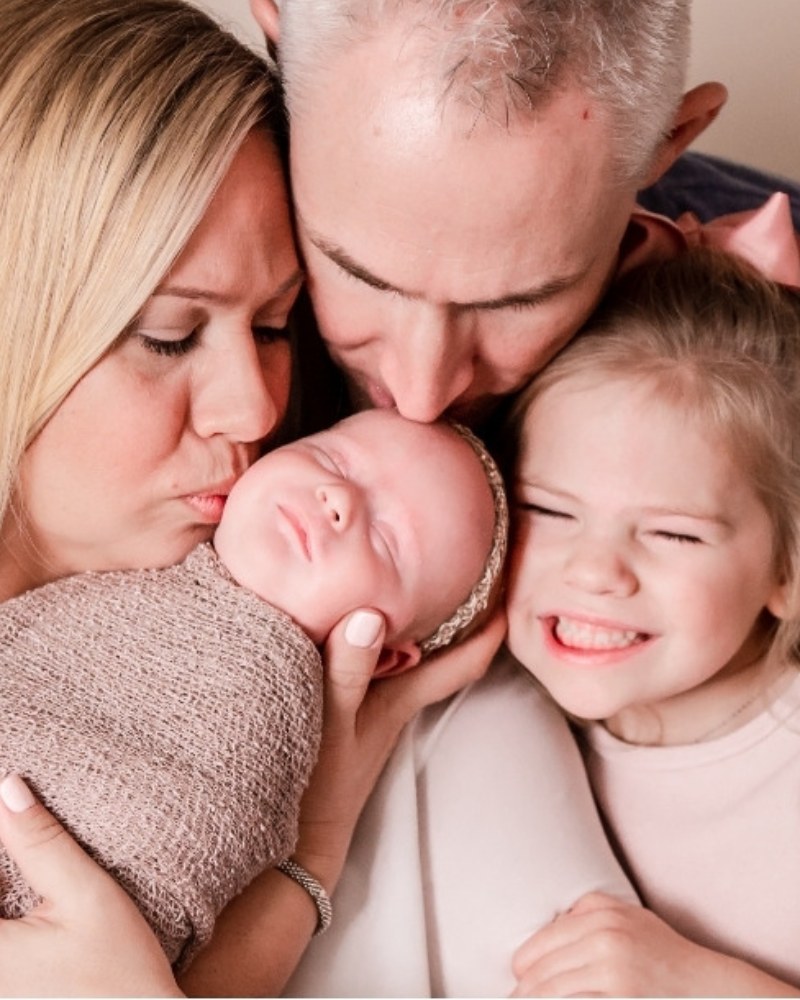 Parents and big sister kissing their newborn