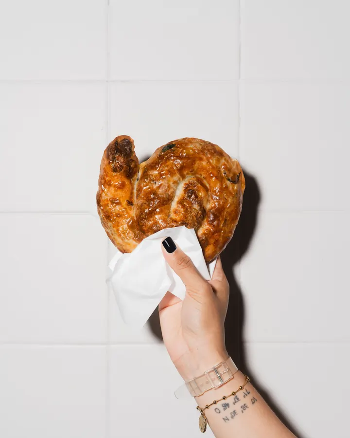 A golden rose börek held up against white tiles