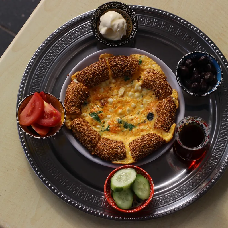 Simit ring filled with baked eggs and cheese, served with olives, tomato, cucumber and Turkish tea