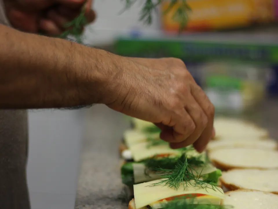 Hands garnishing a tray of catering sandwiches with fresh dill