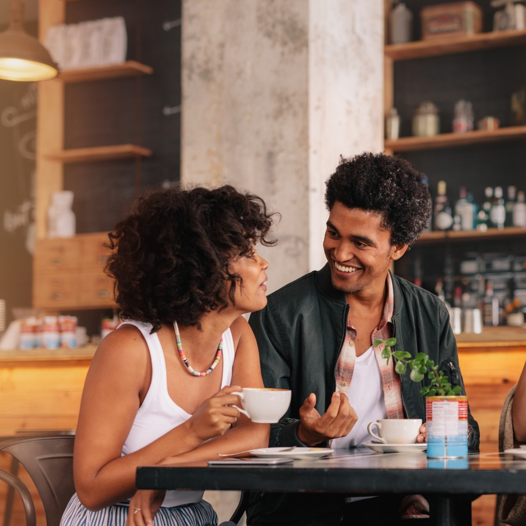 A smiling Shay Bunna barista behind the counter with a cup of coffee