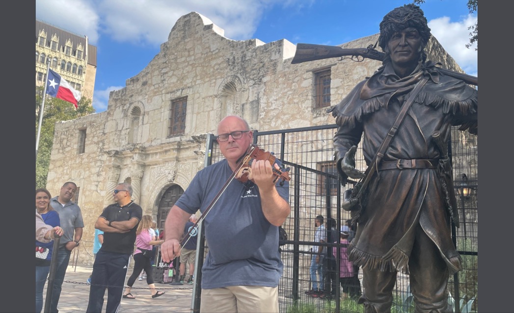 Colin playing fiddle beside the Davy Crockett statue at the Alamo