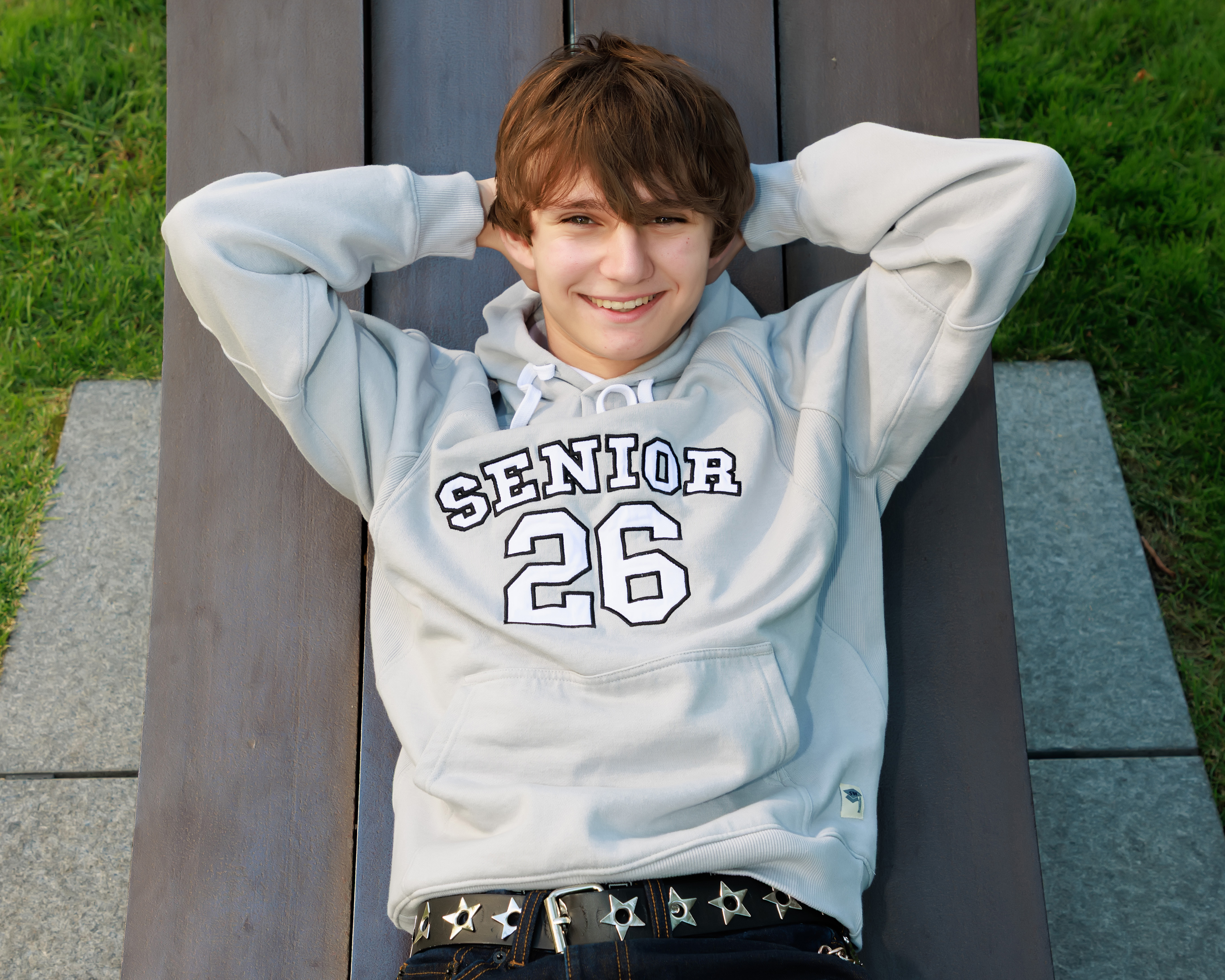 Senior boy in a Senior 26 hoodie lying on a bench with his hands behind his head