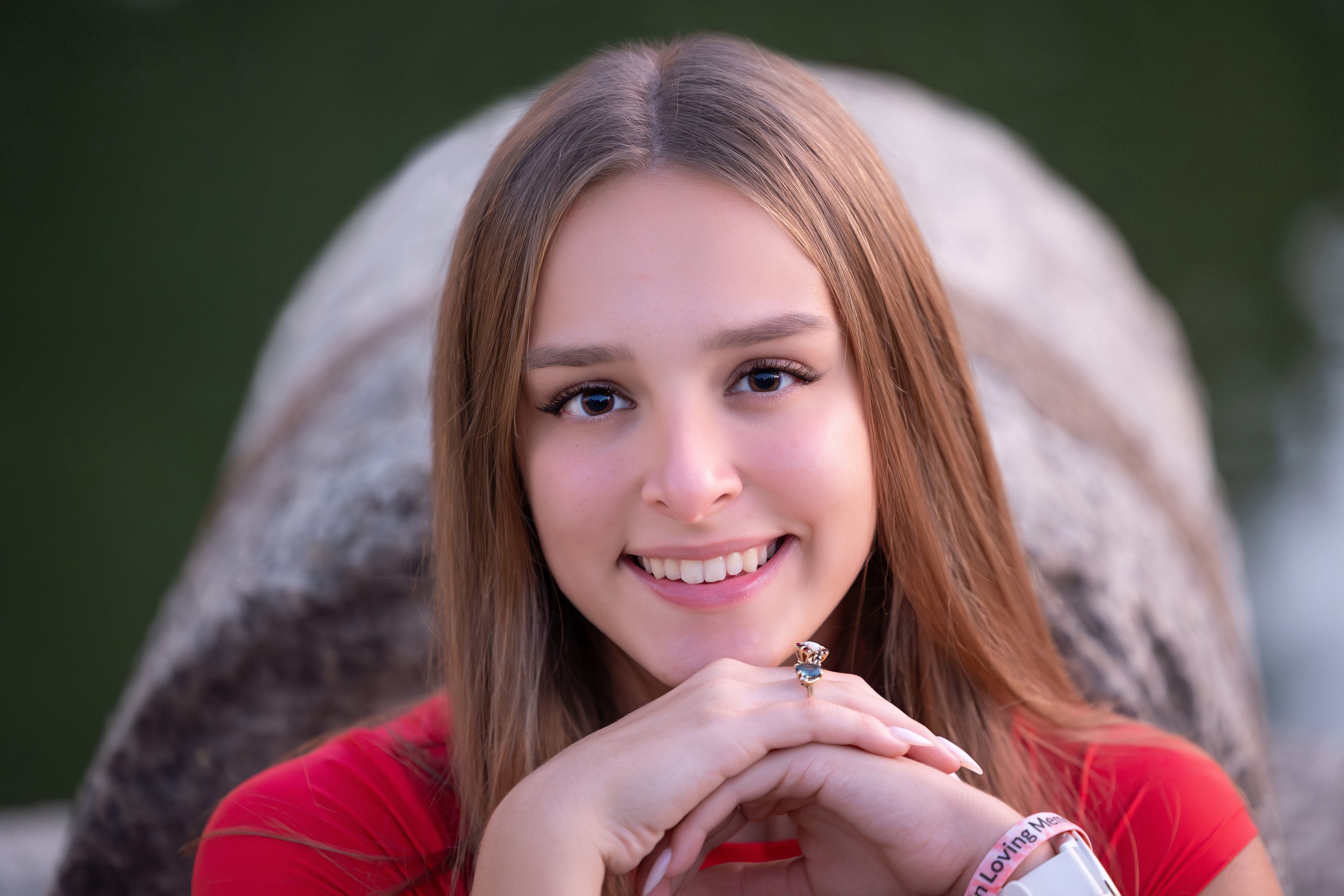Close-up senior portrait of a smiling girl resting her chin on her hands in front of a boulder