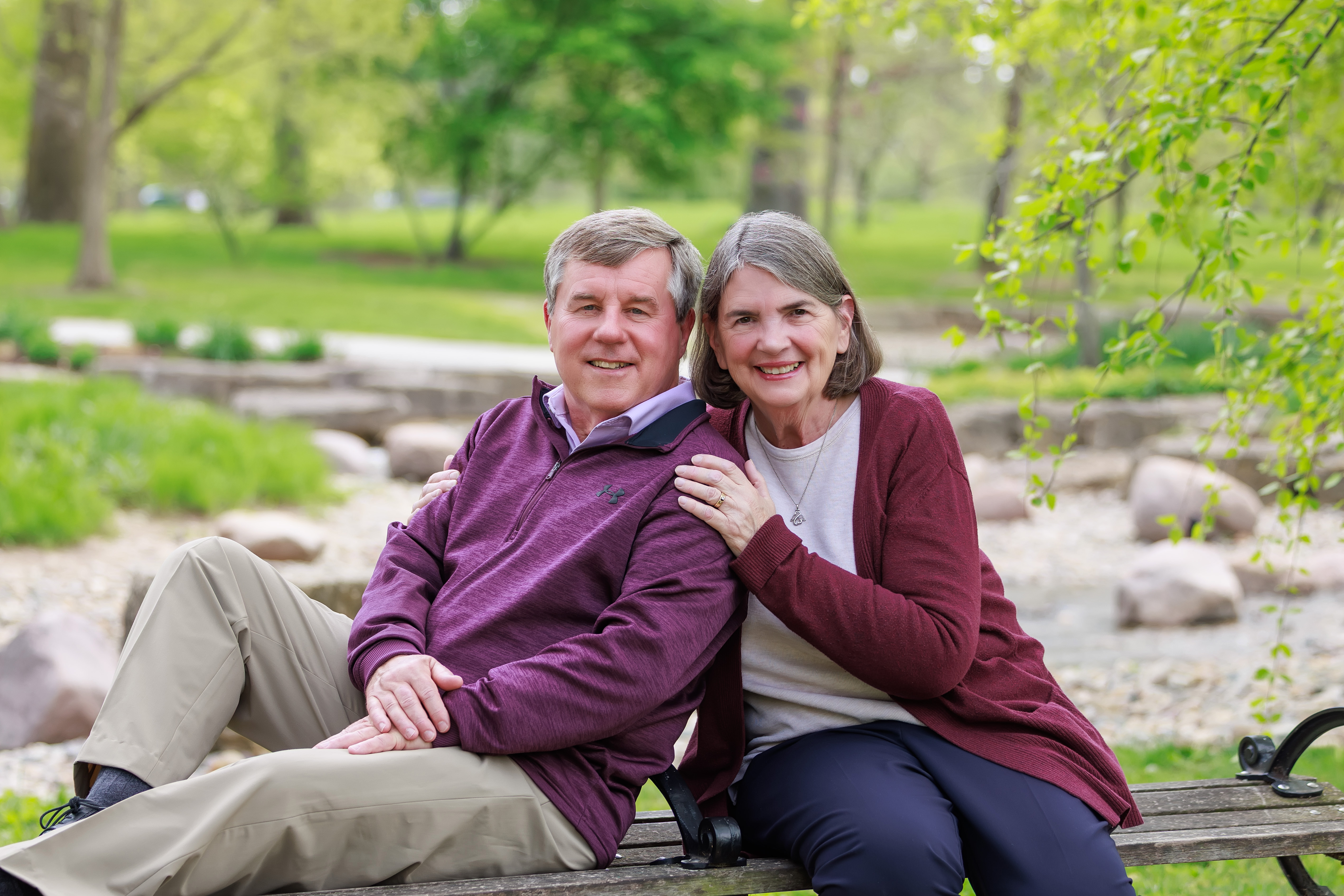 Older couple sitting close together on a park bench, anniversary portrait