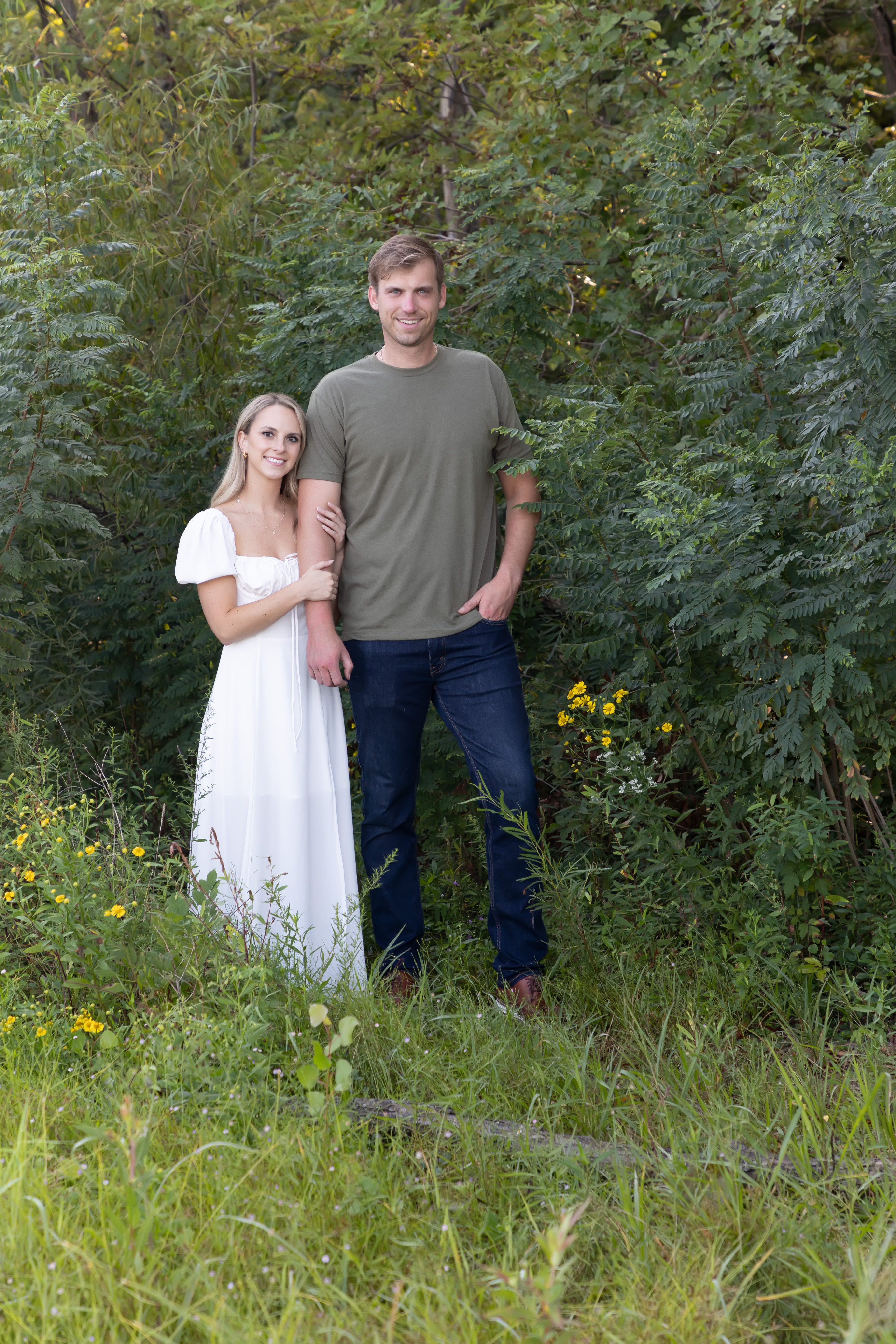 Couple standing close together in front of lush greenery and wildflowers