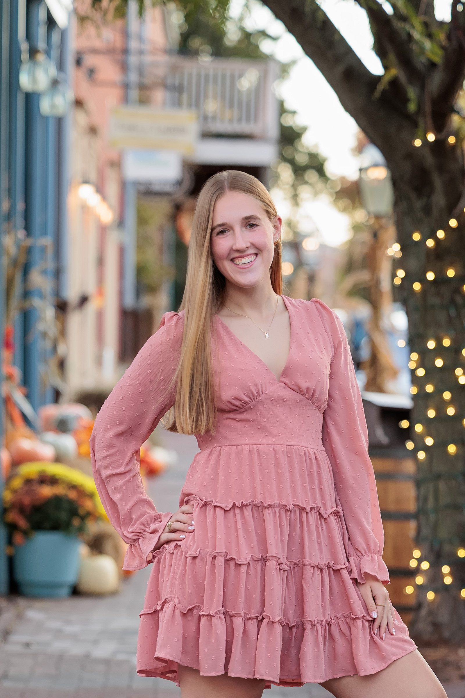 Senior girl in a pink tiered dress on a historic shopping street decorated for fall, St. Louis senior portraits