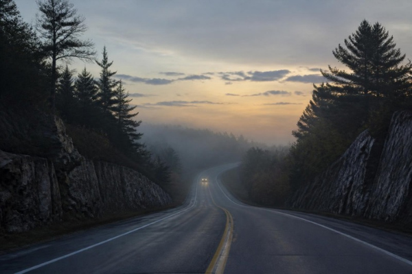 Highway 11 winding through Muskoka rock cuts and pines at dawn