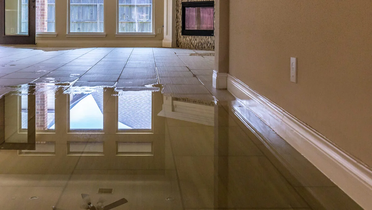 An indoor view of a home with a flooded tile floor reflecting windows and an outdoor scene.