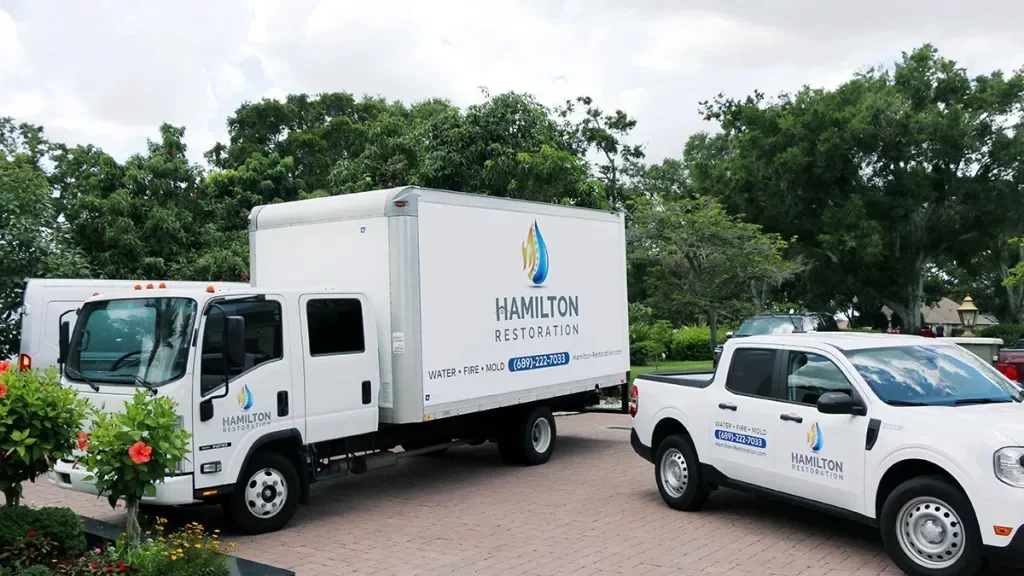 A large white Hamilton Restoration box truck alongside a white Hamilton Restoration pickup truck on a paved drive.