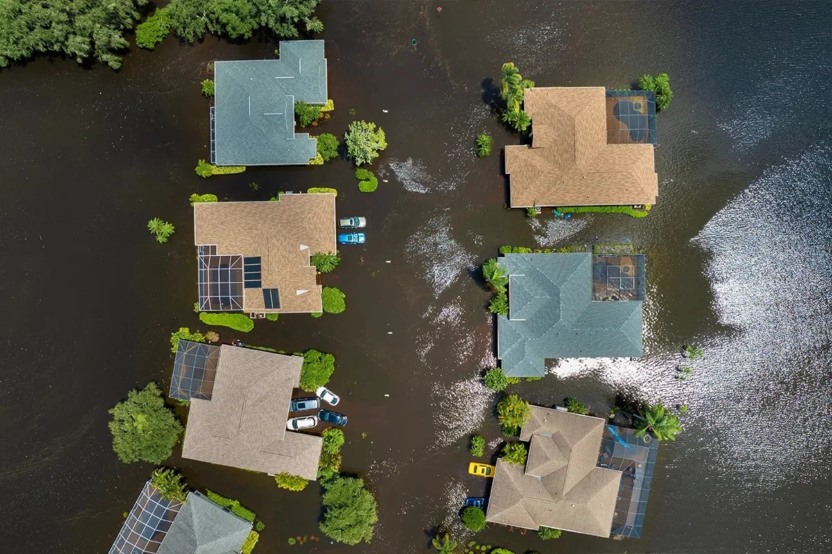 An aerial view shows multiple houses in a flooded suburban community, with dark water covering yards and streets.